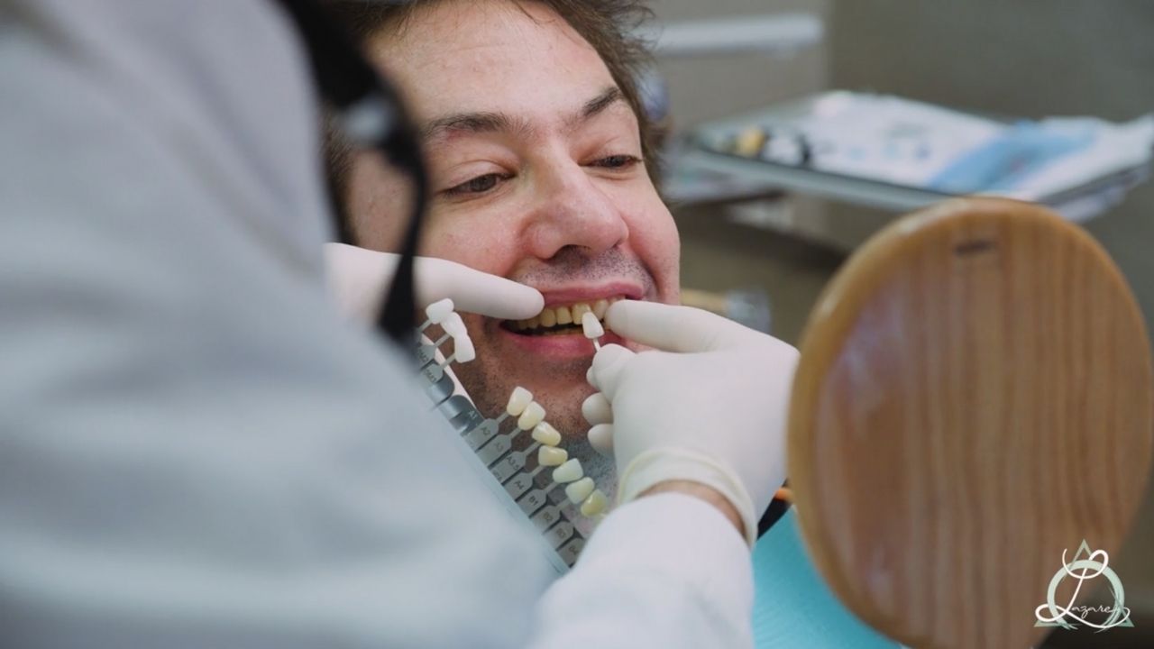 A patient at the dentist's office getting their tooth shade matched for a cosmetic procedure, with the dentist holding a shade guide near the patient's teeth.